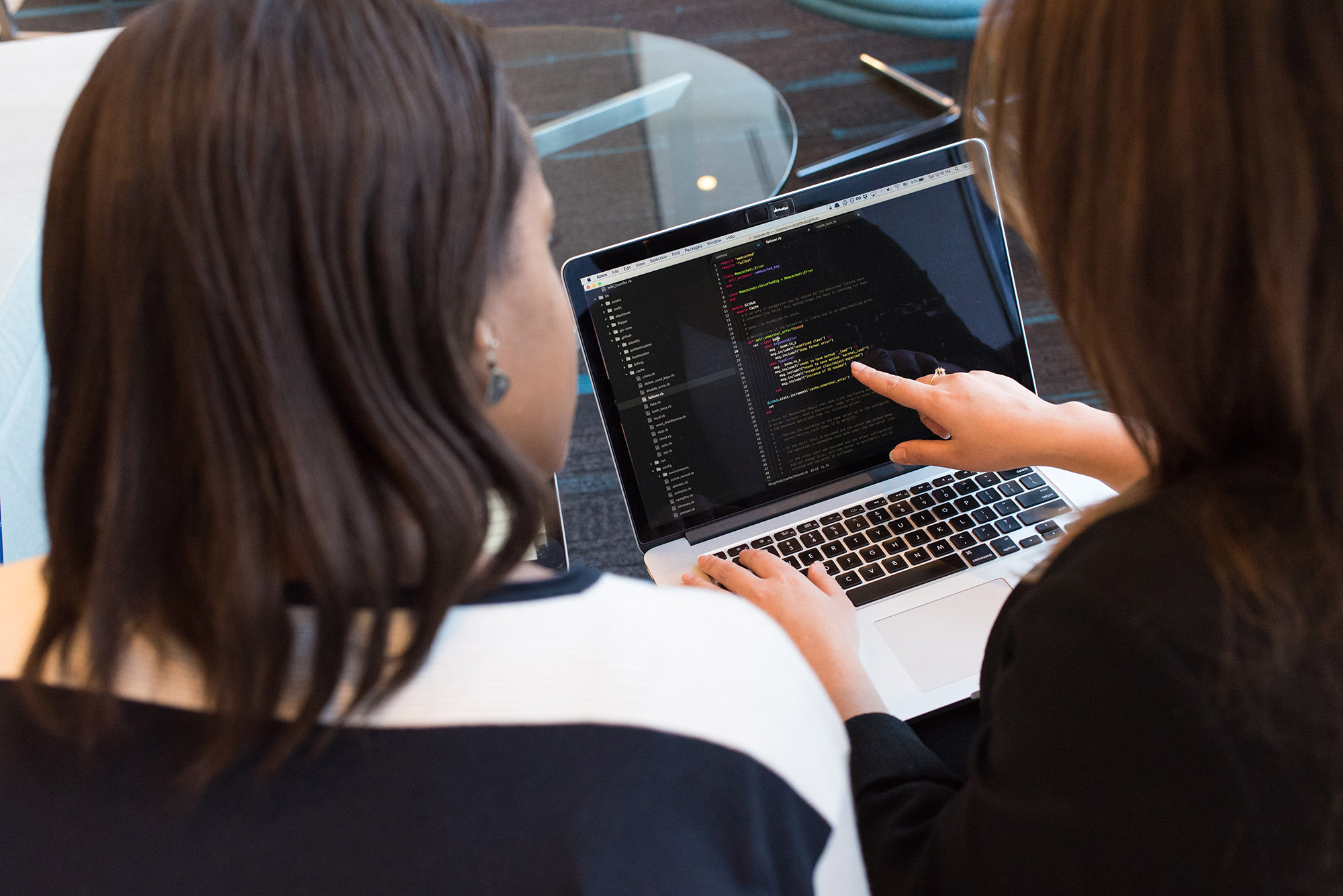 Two women on laptop, one pointing to screen of code