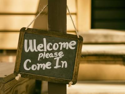 A sign hanging on a post. Sign reads "Welcome, please come in"
