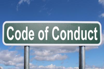 A picture of a highway sign with white letters on a green background spelling code of conduct against a blue sky.