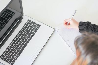 Woman writing on notepad by laptop