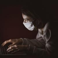 woman in mask works on laptop